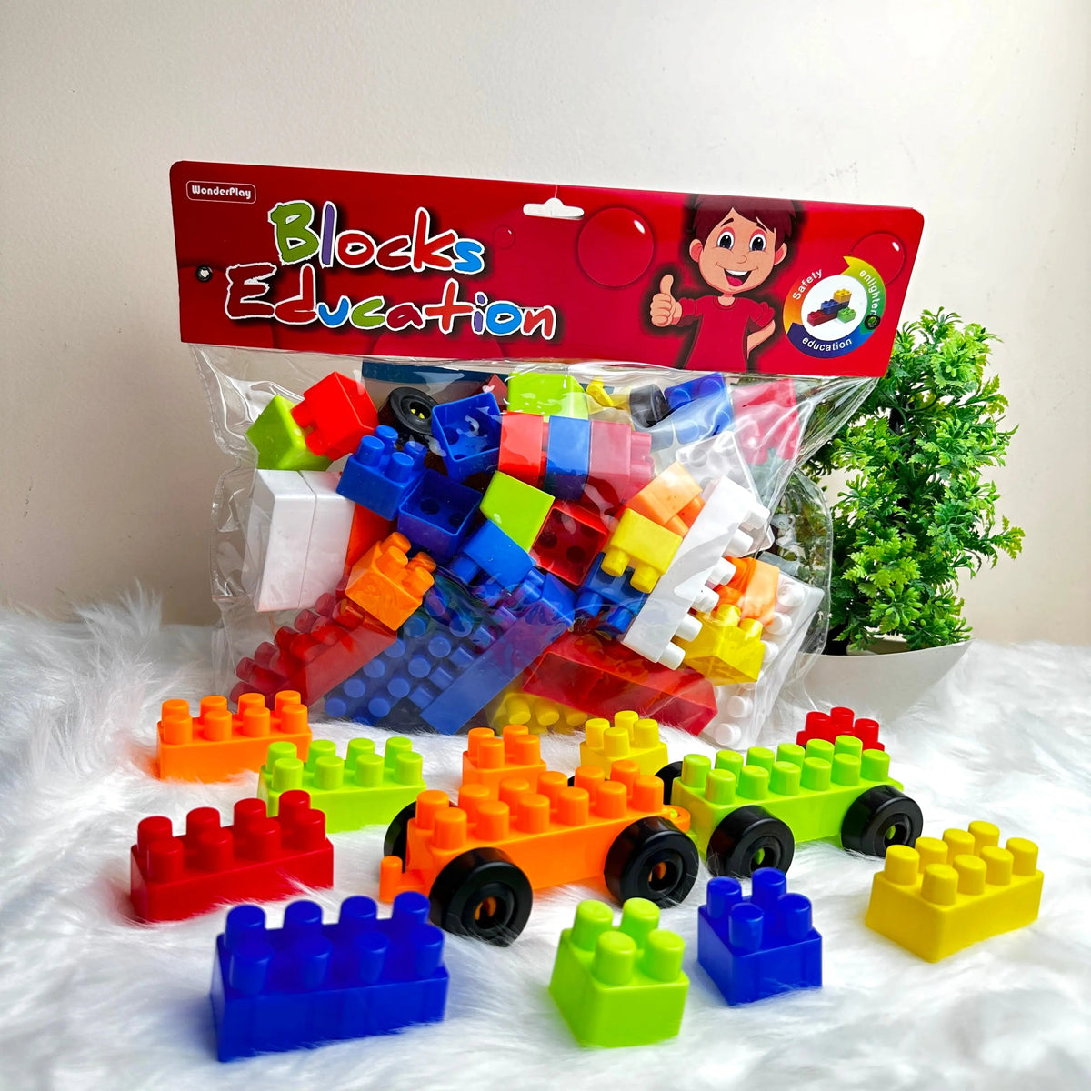 A set of colorful building blocks in various shapes and sizes, displayed in front of a transparent packaging with a 'Blocks Education' label. A few blocks are arranged on a surface, and others are scattered around.