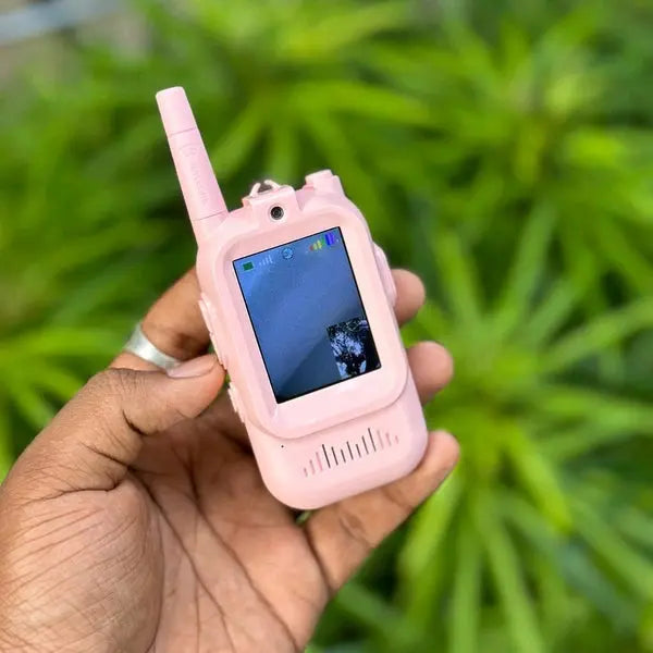 Pink walkie-talkie held in a hand with a blurred green plant background