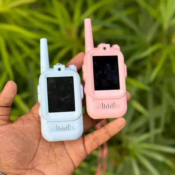 Two toy walkie-talkies, one white and one pink, held in a hand with a green leafy background.