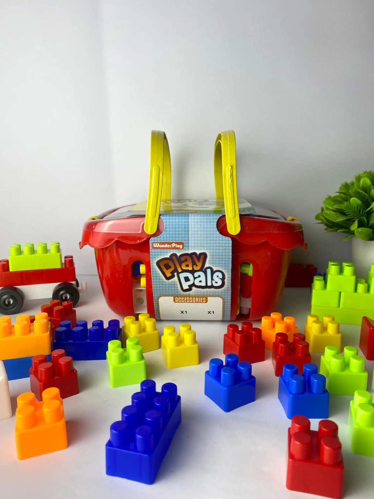 A variety of colorful building blocks spilled out in front of a red briefcase-style container with yellow handles. The container has 'Play Pals' written on it.