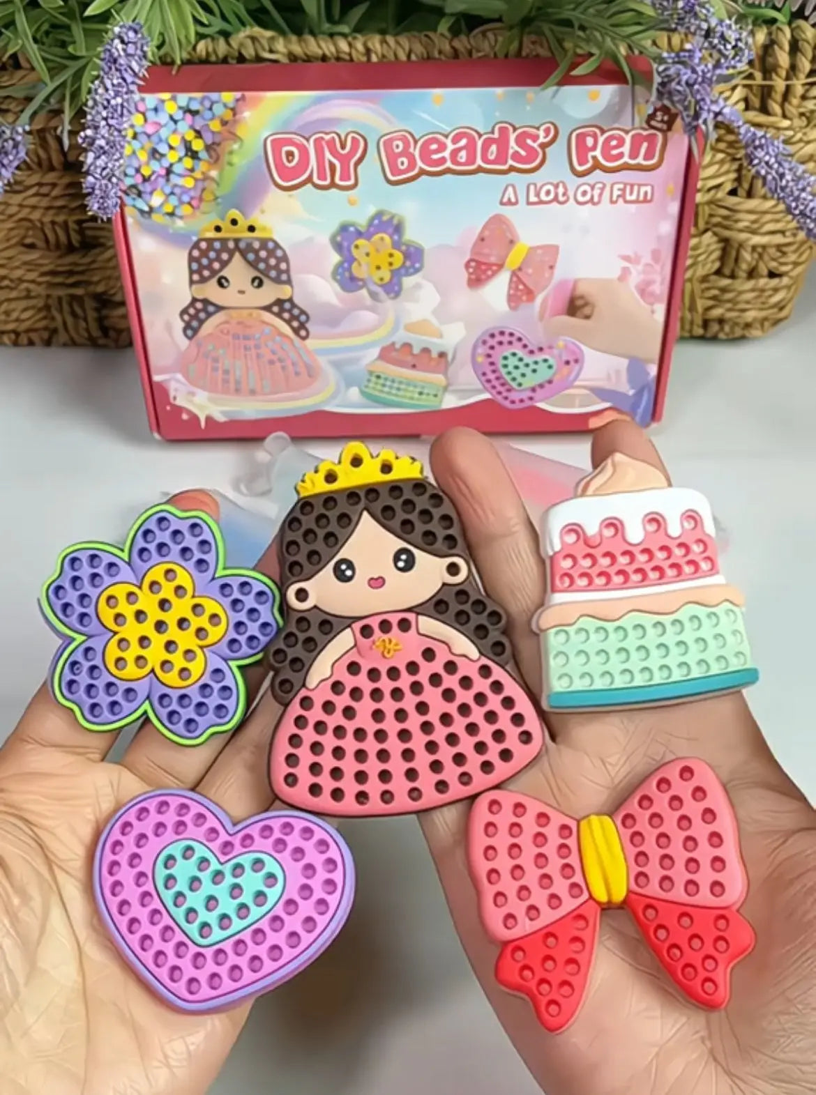 Colorful DIY bead toys including a flower, princess, cake, and bow held by a hand with a box labeled 'DIY Beads Pen' in the background.