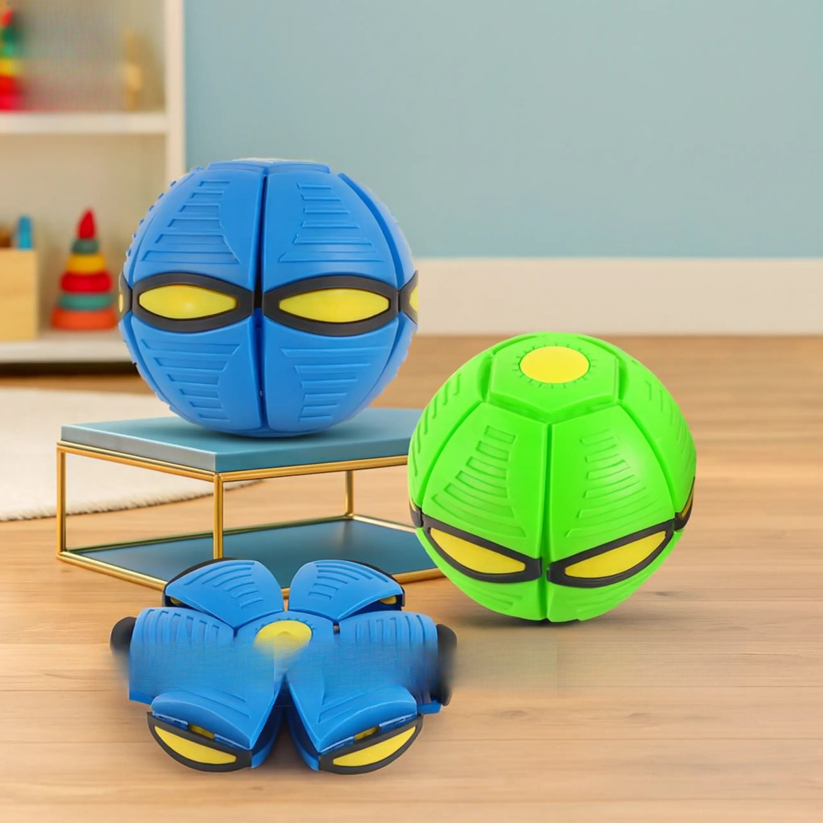 Two transforming toy balls, one blue and one green, on a wooden floor with a colorful background.